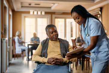 Happy nurse and senior man in wheelchair reading his medical record at nursing home